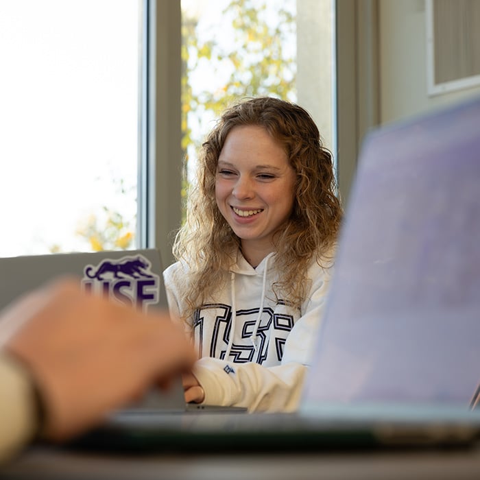 Student smiling in class working on their laptop